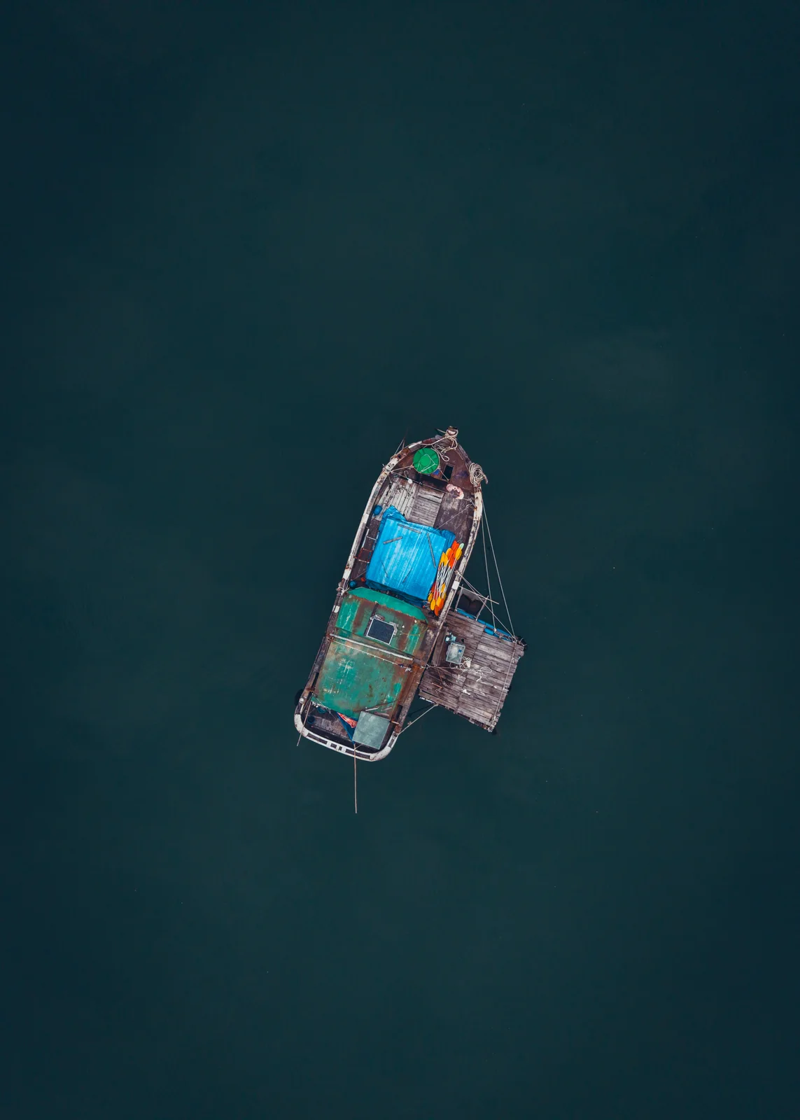 Une barque colorée flotte seule sur une mer d’un bleu profond, vue du ciel.