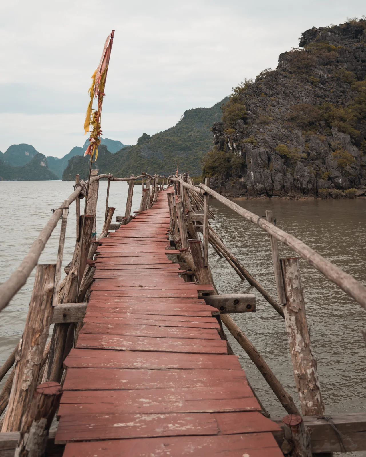 Une passerelle rouge s’avance entre les reliefs d’une baie vietnamienne.