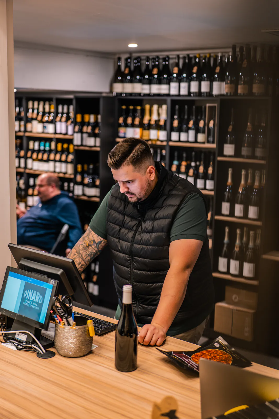 Un caviste se concentre à la caisse au milieu des bouteilles de sa boutique.