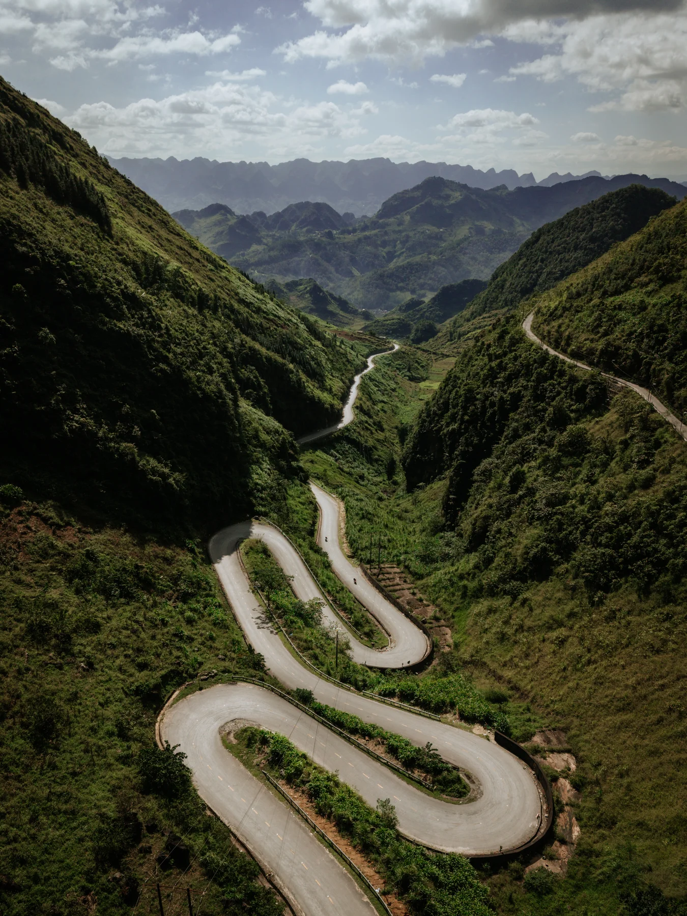 Une route dessine de grands lacets entre des montagnes verdoyantes.