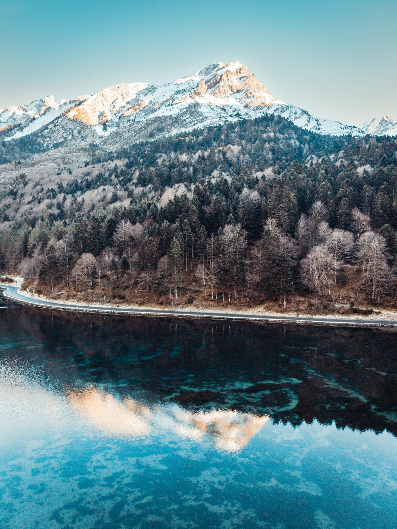 Un lac turquoise reflète une montagne enneigée et une forêt au bord de l’eau.