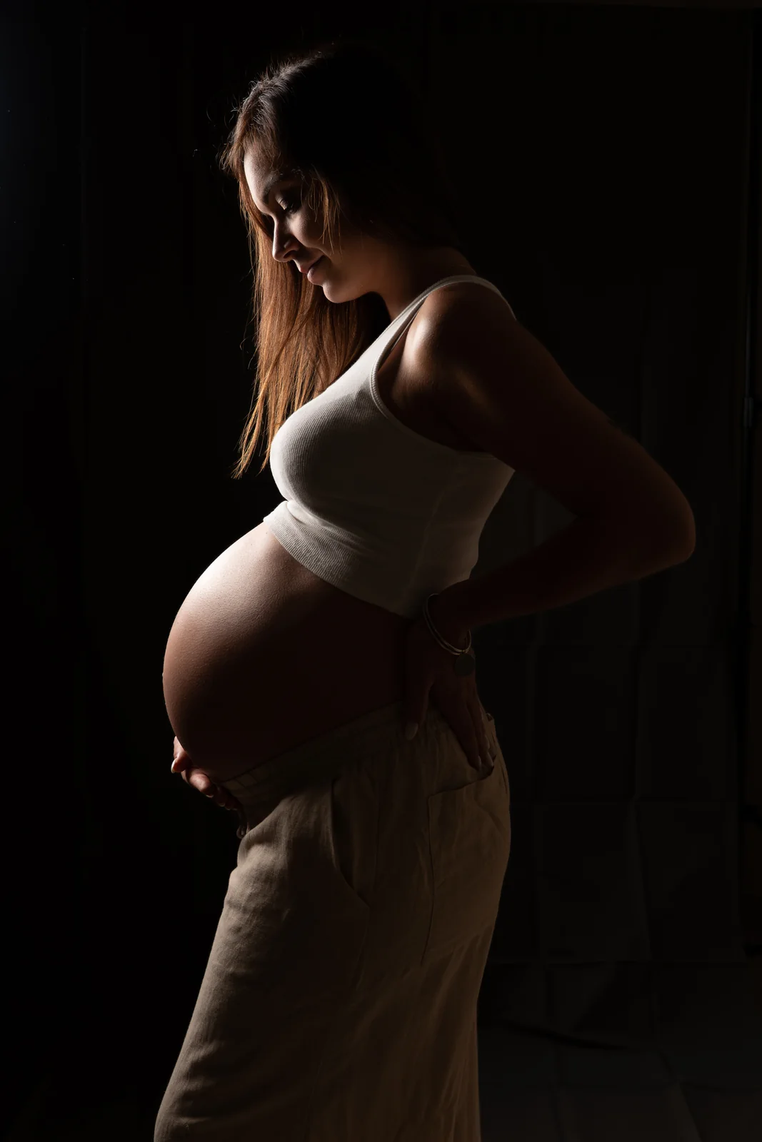 La silhouette d’une future mère se dessine de profil dans une lumière de clair-obscur.