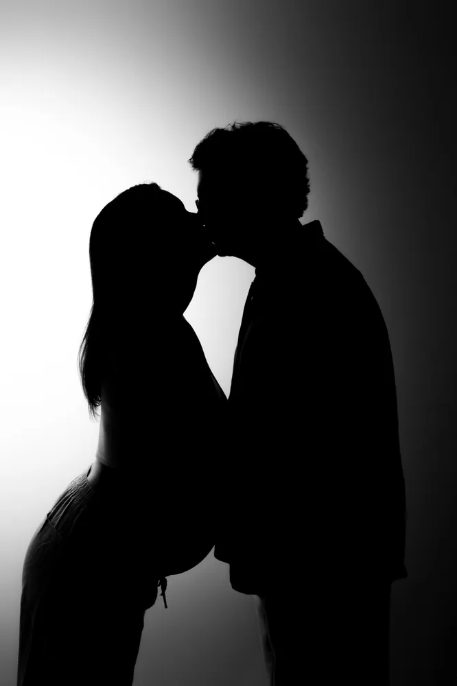 Deux silhouettes s’embrassent devant une lumière en dégradé noir et blanc.