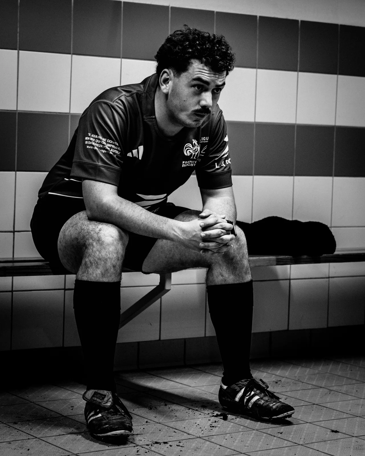 Un joueur de rugby assis dans un vestiaire se concentre avant le match, en noir et blanc.