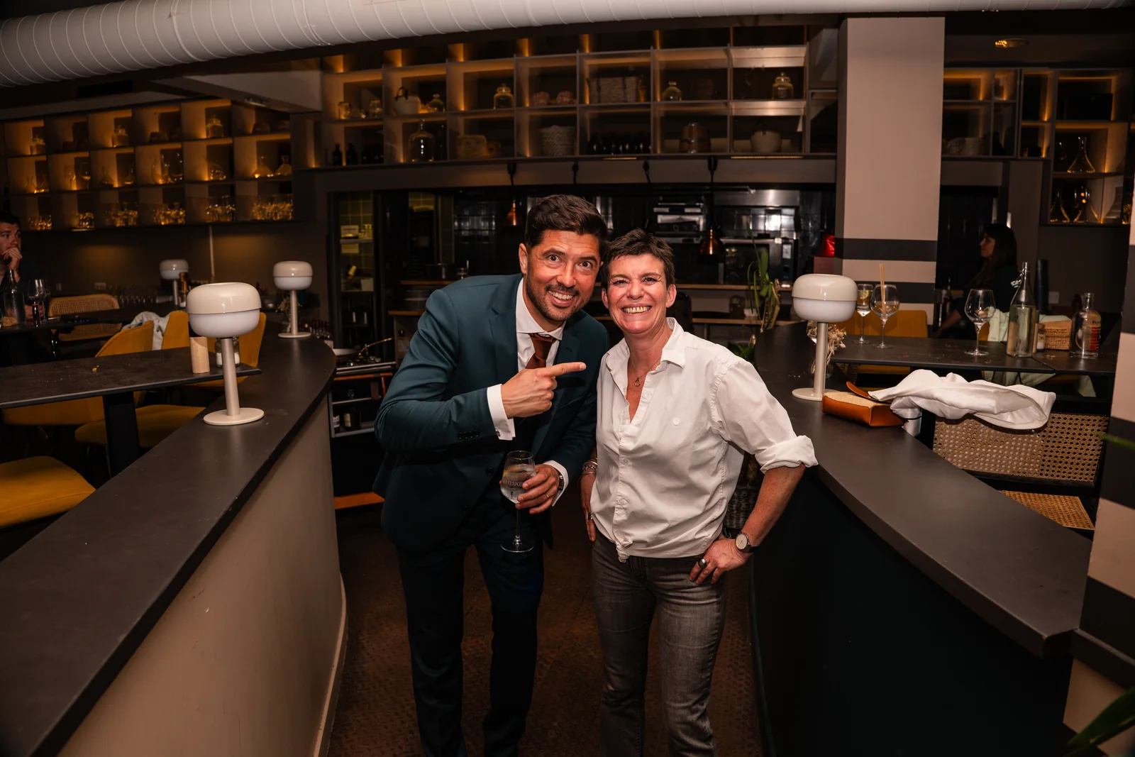 Le marié célèbre la soirée avec une proche devant le bar de la réception.